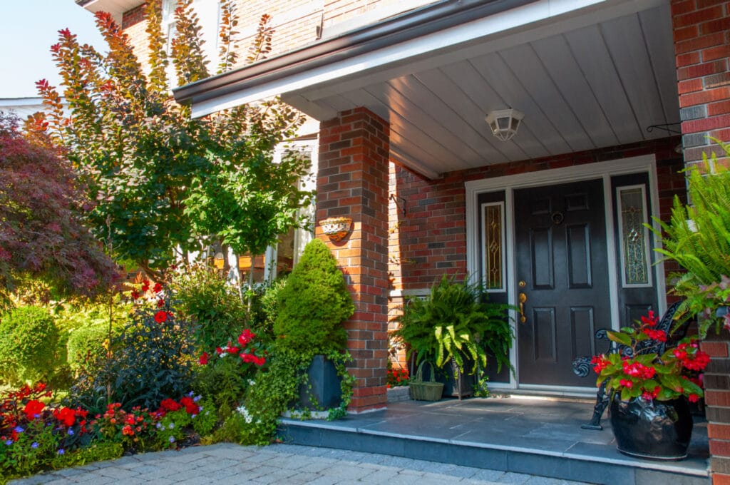 Front door area of a home with black door and red flowers.