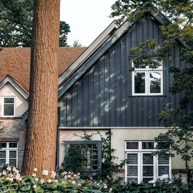 Blue sided home surrounded by floral bushes and tall trees.