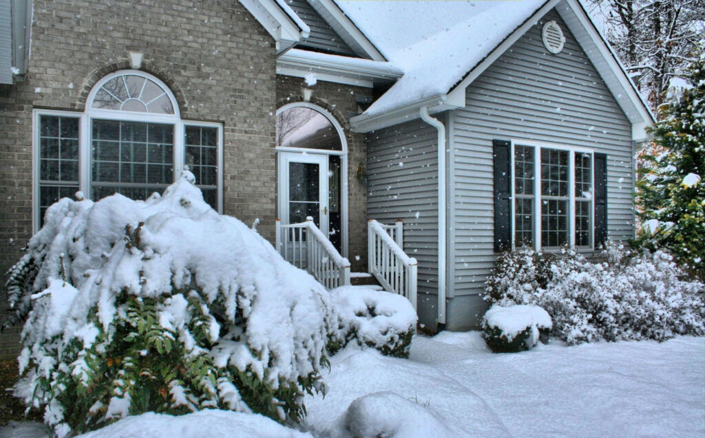 Front of urban home with snowfall and snow coverage.