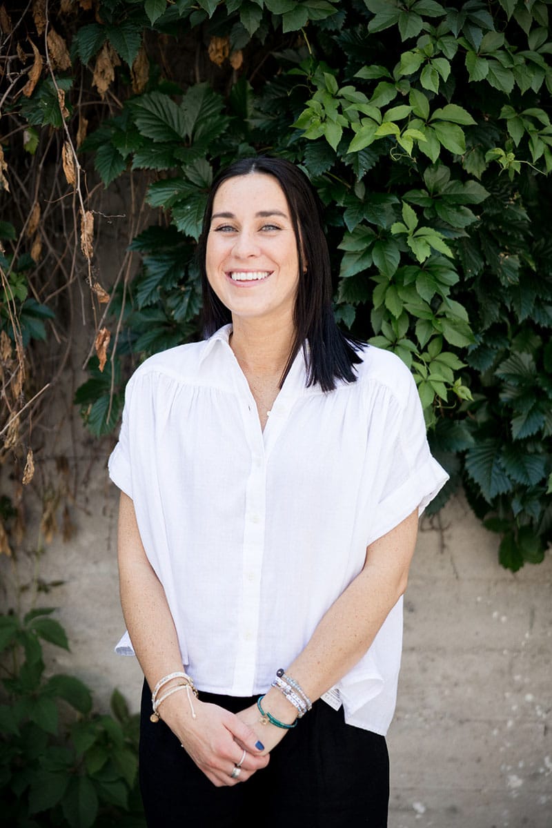 Laura Barrick sitting and smiling up to the camera with dark background.